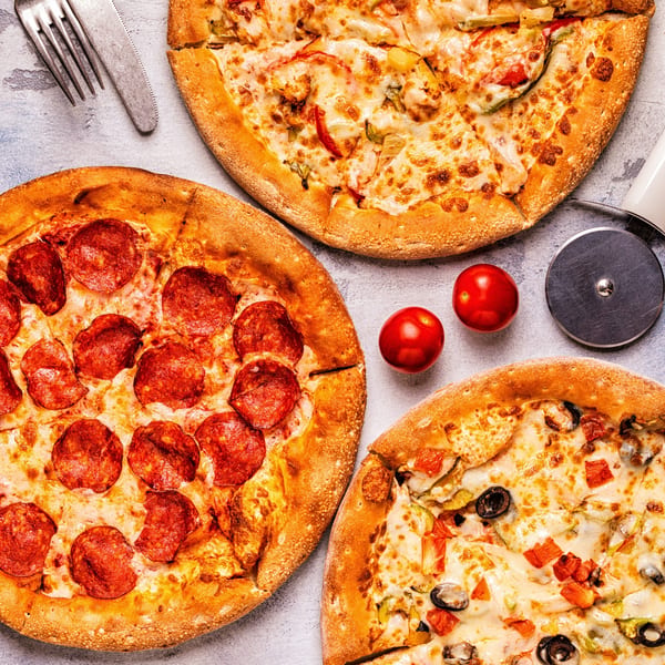 Three SUPPA'S PIZZA & SUBS pizzas, including pepperoni and vegetable, with a pizza cutter and tomatoes.