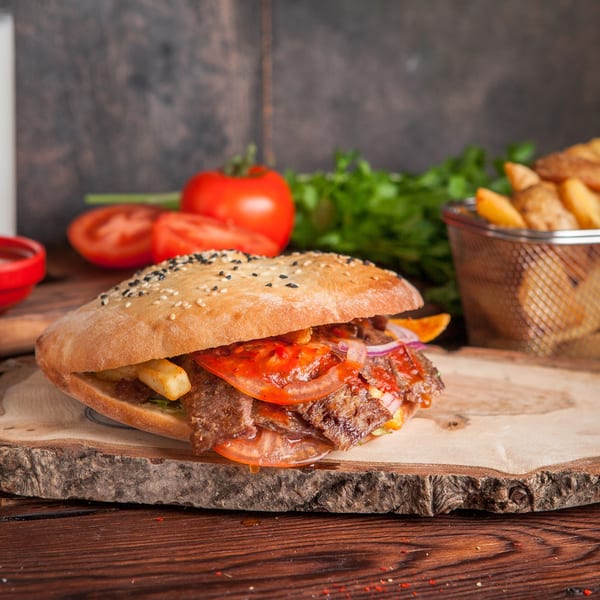 A SUPPA'S PIZZA & SUBS sub sandwich with meat, tomatoes, onions, and fries on a wooden board.