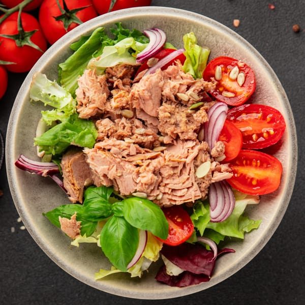 Tuna salad with lettuce, red onion, cherry tomatoes, basil, and pumpkin seeds in a bowl.