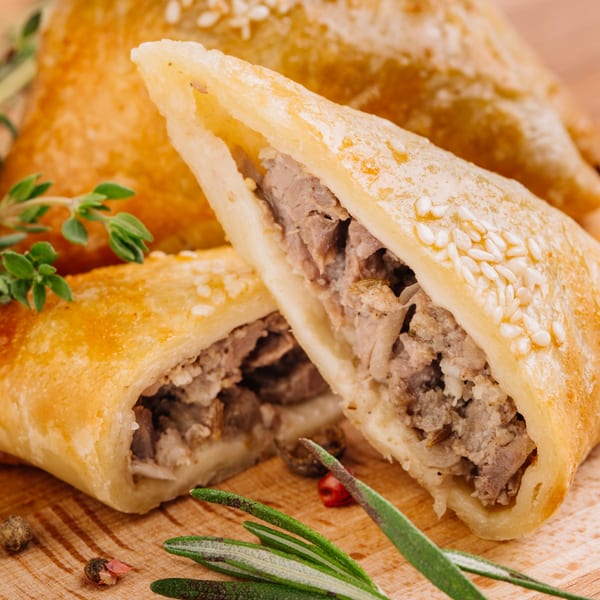 Golden-brown calzones, one sliced open to reveal a savory meat filling, garnished with herbs.