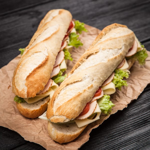 Two SUPPA'S SUBS, turkey and cheese with lettuce and tomato, on brown paper.